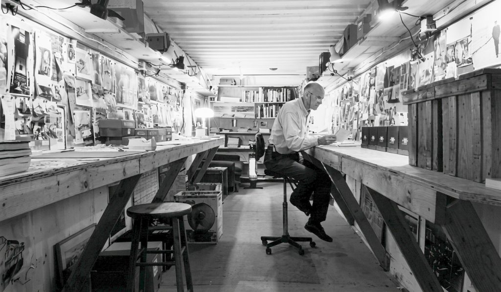 Stewart Brand is using a workspace inside a shipping container to organize his books raw research utilizing little magnets holding up the photos on sheet steel on the walls.